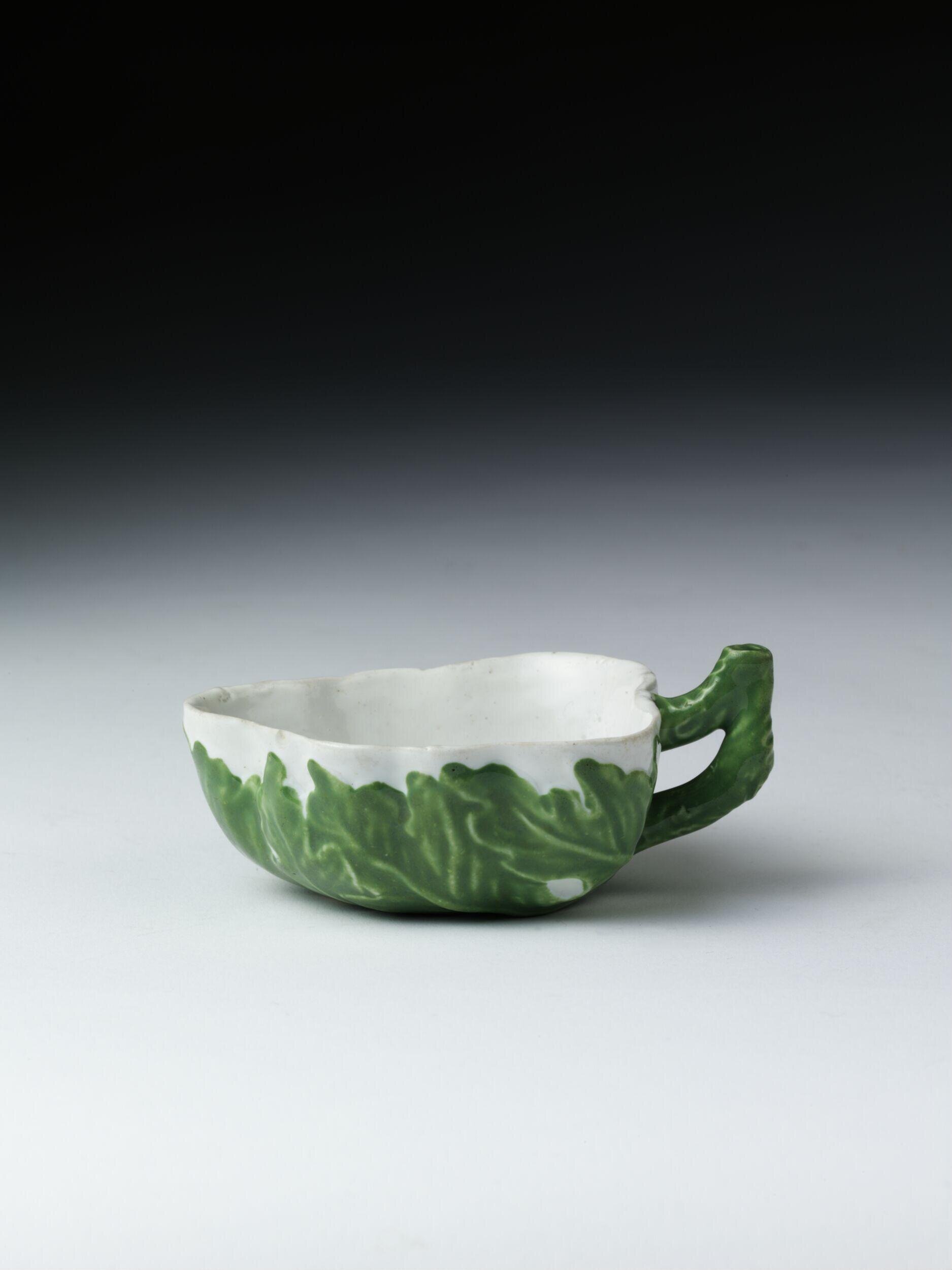 Sweetmeat-tray of hard-paste porcelain painted with enamels and moulded. The outside is moulded in the shape of a leaf with a stalk forming the handle, coloured green. Inside is a formal spray of flowers painted in various colours.