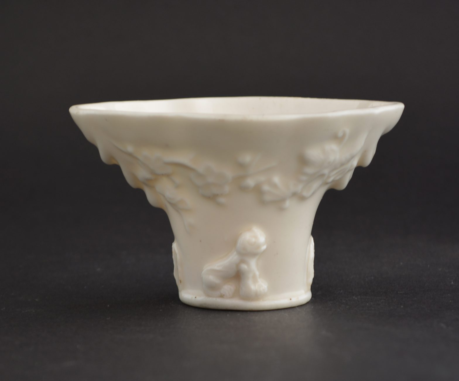 A 17th Century Blanc de Chine `Libation Cup`, Shunzhi or Kangxi Period c.1640-1700, Dehua Kilns Fujian Province. On One Side with Moulded Decoration Depicting a Dragon Emerging from Clouds and a Tiger (Applied) on the Ground Beneath a Flowering Plum (Prunus) Tree. The Other Side with a Crane Flying Above a Spotted Deer (Applied) with a Pine Tree. The Applied Decoration is Crisp and the Branch of the Tree has Been Applied so there is a Part of it that is Separate from the Body of the Cup.