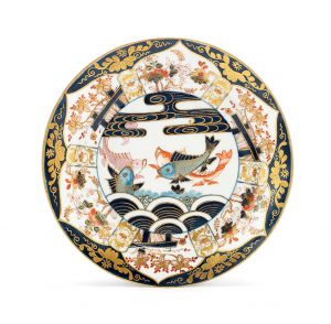  A Worcester plate, circa 1770 Decorated in the Japanese Imari style with four carp swimming among stylised waves, the border richly painted and gilt with petal-shaped panels of flowering oriental shrubs, the blue ground gilt with further scrolling ornament, the underside of the rim painted with three sprays of iron-red flowers, 22.7cm diam 
