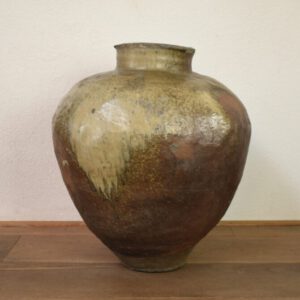 A Massive Japanese Stoneware Ōtsubo, late Muromachi Period 1392 – 1573, perhaps Tokoname ware. This substantial Muromachi jar is made from dense gritty stoneware, it is decorated with a natural ash glaze with pools, splashes and thick running as if by accident down the side of the jar. The surface is, in part unglazed but glaze suspended in the air of the kiln has settled on the surface leave a semi-matt sheen. The areas without glaze have oxidised a red or red-brown due iron oxides migrating to the surface during firing. Ōtsubo Jars like the present example are a perfect reflection of the imperfection of wabi–sabi. The surface, contains lumps, marks where other pieces stuck to it in the kiln, small cracks and a faceted surface in places. This type of pottery surface is, in Japan, seen as a landscape that invites ones eye to walk across its hills, rocks and ravines. The lower part has a line around it caused during the firing, it looks as if this was done by the kiln support holding upright in the glaze firing .These substantial jars were used to store fresh water, the water for the tea ceremony would be collected from Ōtsubo and decanted into smaller vessels.