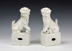 A pair of Chinese blanc de chine figures of Buddhist lions, early Kangxi (1662-1722).The lions are shown seated on rectangular pedestals, each with a forepaw resting on a brocade ball, one with a cub rearing at her side, 30cm. The glaze is of a brilliant grey/white appearance. They appear in the 1688 Burghley Inventory: ‘My Lords Anty Roome … 2 wt Lyons’ are listed under the heading ‘China over ye Chimney.’ 