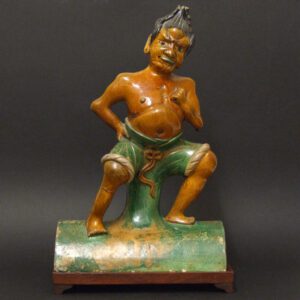 An Inscribed Ming Lead-Glazed Pottery Roof-Tile in the Form of a Demon, Probably Shanxi Province, Late Ming c.1500-1640. Shown on as an Ugly Muscular Semi-Human Figure Squatting on Top of a Convex Ridge-Tile, his Trousers are Rolled up and Tied with a Sash, his Fat Belly Protruding Over the Top . His Mad Demonic Face has a Fixed Stair and His Green Tongue is Poking Out. His Ears are Pierced and Would Probably have had Metal Earrings, the Hand he has Clasped to His Chest is Also Pirced and Would Probably Held a Metal Weapon. The Ridge Tile is Inscribed Beneath the Glaze with a Large Single Character.