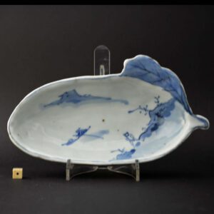 An unusual Ming porcelain dish for the Japanese market, Tianqi or early Chongzhen c.1625 – 1635. The thickly moulded porcelain tea ceremony dish is in the shape of an aubergine. It is painted with a simple landscape including a small vessel on the water and a solitary figure on the foreshore.SOLD Condition No damage but with some small bubbles to the glaze on the reverse. Size Length : 19 cm (7 1/2 inches) Provenance N/A Stock number 24662