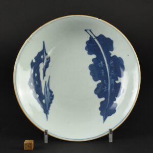 A 17th Century Chinese Blue and White Porcelain Saucer Shaped Dish, Shunzhi or Early Kangxi c.1650 – 1670, Jingdezhen Kilns. The poem on this dish has been translated for me ; Always a flower with bird chirping, while silence goes with fallen leaves (thank you to S.N.). Poem dishes of this type, painted with a leaf next to a taihu rock were made during the reign of Shunzhi (1644-1661), with variations carrying on until the early Kangxi period c.1662 to 1670. See below for a Kangxi dish we sold some years ago that came from Marchant & Son, which is dated 1667. A number of these later smaller dishes are known, another dated 1667 is in the Butler Collection (see references). The present example is closer to, but not the same as the two from the Butler Collection, dated to Shuzhi (see references). A considerable numbers of these dishes are in the Palace Museum in Beijing, suggesting they were made for the domestic market, an early example is in the Palace Museum examples, dated to 1648. Indeed, they do not seem to appear in early European collections. The leaves vary from dish to dish, clearly representing different tree species. A second example, in the Butler Collection (III.3.35), specifically mentions a Wutong leaf in the poem. The inscribed poems on these dishes were done by using a wax resist technique. The cobalt pigment would not adhere to the wax characters, it would be burnt off during the firing after glazing leave the white characters we see today. Dishes of this type with designs with poems and symbolism must have appealed to the Scholar class in China. As with other Shuzhi porcelain of this type the glaze has a distinct blue green tinge.SOLD Condition One small rim chip. Some unevenness to the rim. Size Diameter : 19.9 cm (8 inches) Provenance N/A Stock number 25757 References For two dishes of this type dated to the Shuzhi period (1644-1661) see : Leaping The Dragon Gate, The Sir Michael Butler Collection of Seventeenth Century Chinese Porcelain (Teresa Camepa and Katherine Butler, Ad ILissvm. 2021. ISBN 978-1-912168-16-3) Page 287, III.3.34 and III.3.35. For a similar slightly later version, Kangxi blue and white porcelain dish dated 1667, from the Butler Family Collection (collection number F22) see : Seventeenth Century Jingdezhen Porcelain from the Shanghai Museum and the Butler Collection.