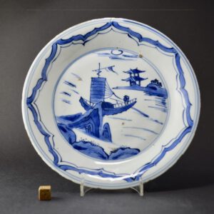 A Ming Blue and White Porcelain Dish, Tianqi (1621-1627) or Chongzhen (1627-1644) dating to c.1630. This Transitional porcelain dish was made for the Japanese market and would have been used to serve food during the Tea Ceremony. It depicts a Chinese vessel navigating its way around jagged rocks, in the distance is a promontory with a two story building at the waters’ edge.SOLD Condition There is a fine rim crack c.25mm. There is a firing crack to the rim and pieces of kiln grit in the glaze. Typical rim fritting. Size Diameter : 20.7 cm (8 1/4 inches). Provenance The James Randolph Hillard MD Collection of Chinese Ceramics for the Japanese Market. Label to the base, Collection number 80. Stock number 25175