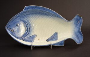 An 18th Century Japanese Porcelain Dish in the Form of a Sea-Bream. The Moulded Form is Painted in Broad Brush Strokes of Dark Cobalt Blue Using a Wet Brush. The Blue has Settled Between the Scales. The Lower Area of the Fish has a Feint Orange Lustre Wash, Gilding has Been Employed to Delineate the Gills, Eyes, Mouth and Some of the Scales. The Base with a Ming Four Character Mark.SOLD Condition There is a small chip repaired with a black filler to the top of the caudal fin (tail) c.9 x 3mm. Size 26 cm (10 inches) Provenance N/A Stock number 22414 References For a very similar Japanese blue and white porcelain fish dish dated to c.1690-1730 see : Complete Catalogue of Shibata Collection (Kyushu Ceramic Museum,2003) page 325, plate 2542. For a similar Japanese Porcelain dish see : The Catalogue of The Shibata Collections, The Exhibition (1) (Akihiko Shibata and Yuko Shibata and others, The Kyushu Ceramic Museum, 1990) Page 153 plate 397. For anothers Japanese porcelain dishes of this type but with gilding see our `Sold Items` 21748, 21749, 22455. For a Japanese celadon glazed porcelain fish dish dated to c.1750-1780 see our `Sold Items` number 20433.
