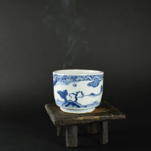 A Rare Ming Blue and White Porcelain Bowl, Tianqi or Chongzhen Period c.1625 – 1640. This bowl was probably used as a Charcoal Container. Once filled with ash, the container would have held pieces of burning charcoal which could be used to light a pipe. In early 17th century Japan tobacco became fashionable with tea drinker. A charcoal container with Japanese pottery pipes as well as a tray for holding them together with a container for loose tobacco would be placed in the waiting room for use before the tea ceremony. Sen no Rikyū (1522-1591) one of Japan’s leading tea masters was known to have possessed such a bowl, it was probably Japanese pottery as there don’t appear to be extant Chinese charcoal burners from the 16th century. This thickly potted Ming container was made for the Japanese market and perfectly reflects Japanese Wabi-Sabi taste – imperfect, humble and desolate (see below). The bowl is uneven, veering towards oval, the rim is heavily fritted, tool marks left by the potter are clearly visible under the thick glaze. A small v-shaped repair appears to have been done by the potter prior to glazing (see close-up photograph). The well is full of kiln grit as well as iron oxide stains. The scene is of a sparse undulating landscape, only populated by two solitary figures, one with a long fishing rod, the other perhaps holding parasol. There is a small building partly obscured by trees or shrubs near a half dead willow tree. The border is in the style of brocaded fabric. Despite being almost oval, this Ming container sits on a circular foot. The Chinese would, I think, have found it curious that the Japanese would order such an odd ‘crude’ bowl. After all they could have made it so much ‘better’ and yet the instructions from Japan would have been to make it imperfect.SOLD Condition There is are two long cracks from the rim to just above the well of the container. Size Diameter 13.2 cm and 11.7 cm (5 1/4 and 4 1/2 inches) Height 9.3 cm (3 3/4 inches) The thickness of the rim c.8 mm. Provenance