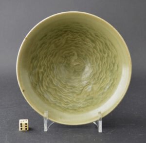 A small Yaozhou Celadon bowl from the Yaozhou kilns in Shaanxi or Henan Province, Northern Song (960 – 1127) or Jin dynasty (1115 – 1234). The conical shaped bowl is crisply moulded with fish among waves, the well of the bowl has another creature, perhaps a turtle. The exterior is cut with lines radiating from the foot to the rim.