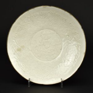 A Fine Moulded Ding Ware Dish, Ding Kilns, Hebei Province, Jin Dynasty, 1115 – 1234. From the collection of Nicholas de la Mare Thompson (1928-2010). This Dingyao (Dingware) Dish is crisply moulded and covered with a thin creamy glaze that do not obscure or diminish the fine bas-relief detail. The shape of this shallow dish uses six small indentations to suggest the shape of a flower, the small indentation to the rim line up with incised lines on the reverse.