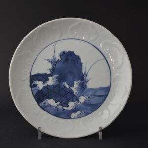 An early Japanese Porcelain dish, Arita kilns c.1660-1670. The finely potted dish is decorated in shallow relief with a repeated ‘Ruyi’ head to the cavetto. The central scene is of waves crashing against two large boulders bound with rope and a rocky outcrop with plants growing from it. The base of this blue and white porcelain dish is marked.SOLD Condition In perfect condition. Size Diameter : 20.3cm (8 inches). Provenance From a Private English Collection of 17th Century Japanese and Chinese Porcelain. Stock number 25098