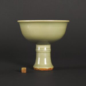 A Fine Yuan or Early Ming Dynasty Celadon Ware Stem Bowl, Longquan kilns, Zhejiang Province. The flared cup with everted rim raises from a stem based on a section of bamboo. The interior is incised with loose scrolling lotus and the well of the stem bowl is decorated with an impressed roundel of an open flower with four pairs of leaves. The base is conical and the robust cut foot is burnt brown-orange due to iron oxide migration to the surface during the glaze firing. The fragment of a Yuan or Ming Longquan kiln stem bowl shown in the photographs is a kiln waster – Robert McPherson Antiques Reference Collection (not for sale).SOLD Condition In excellent condition, numerous fine glaze scratches. Firing fault - a tiny spot on the rim is fired brown-orange due to the glaze not covering the edge completely. Size Height 13.5 cm (5 1/3 inches) Provenance From a Private Collection Stock number 25815