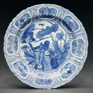 A MOLDED BLUE AND WHITE 'KRAAK PORSELEIN' DISHLATE MING DYNASTY, CIRCA 1610-1630 The dish has a bracket-lobed rim and is finely decorated in vibrant tones of cobalt blue with a central scene of a duck in a lotus pond enclosed by radiating lappets containing floral groupings and flying insects. The reverse is decorated with similar lappets and a small 'egret' mark on the base. 8 ½ in. (21.6 cm.) Provenance Blitz Antiek, Amsterdam, 1989. Collection of Julia and John Curtis.
