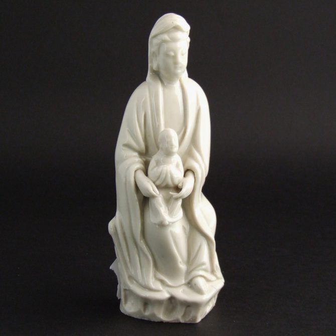 A Late Ming or Early Qing Dynasty Blanc de Chine Porcelain Model of Guanyin and Child, Dehua Kilns, Fujian Province c.1630-1660. Guanyin is Shown Seated on Rocks, Her Serene Face Looking Directly Ahead While She Perches a Child on Her Right Knee. Guanyin`s Back and the Back of the Rocky Seat Show Clear Signs of a Finishing Tool Being Used, as if a Paring Knife Had been Used. The Colour is a Rich Dark Cream.Condition In very good condition, Guanyin's thumb has lost c.2 to 3 mm and one of the tips of her finger is missing c.1 or 2 mm. Size Height : 16.5 cm (6 1/2 inches). Stock number 23568