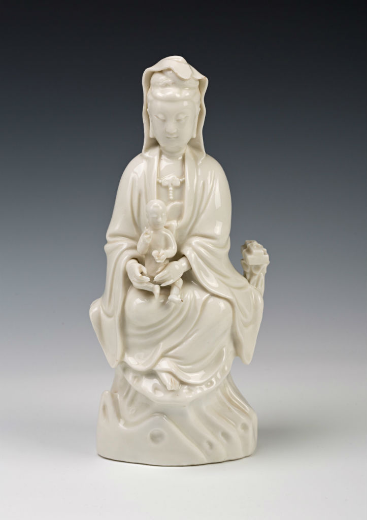 A pair of Chinese blanc de chine figures of Guanyin, late 17th Century.Each robed figure has a small child seated in her lap, with auspicious objects to one side, 29.5cm. A granter of benefits and mercies and a helper on the path to Enlightenment, Guanyin appears here as the giver of children. The figures appear in the 1690 Devonshire Schedule, an inventory itemising an extraordinary bequest from Elizabeth, Countess of Devonshire (1619-1689), to her daughter Anne, Countess of Exeter (1649-1700). They are listed as: ‘two large white Ffigures with children in their lapps.’ In the West, figures of Guanyin, Bodhisattva of Compassion, were perhaps the most popular of all the products from the Dehua kilns. REFERENCE: CER0087