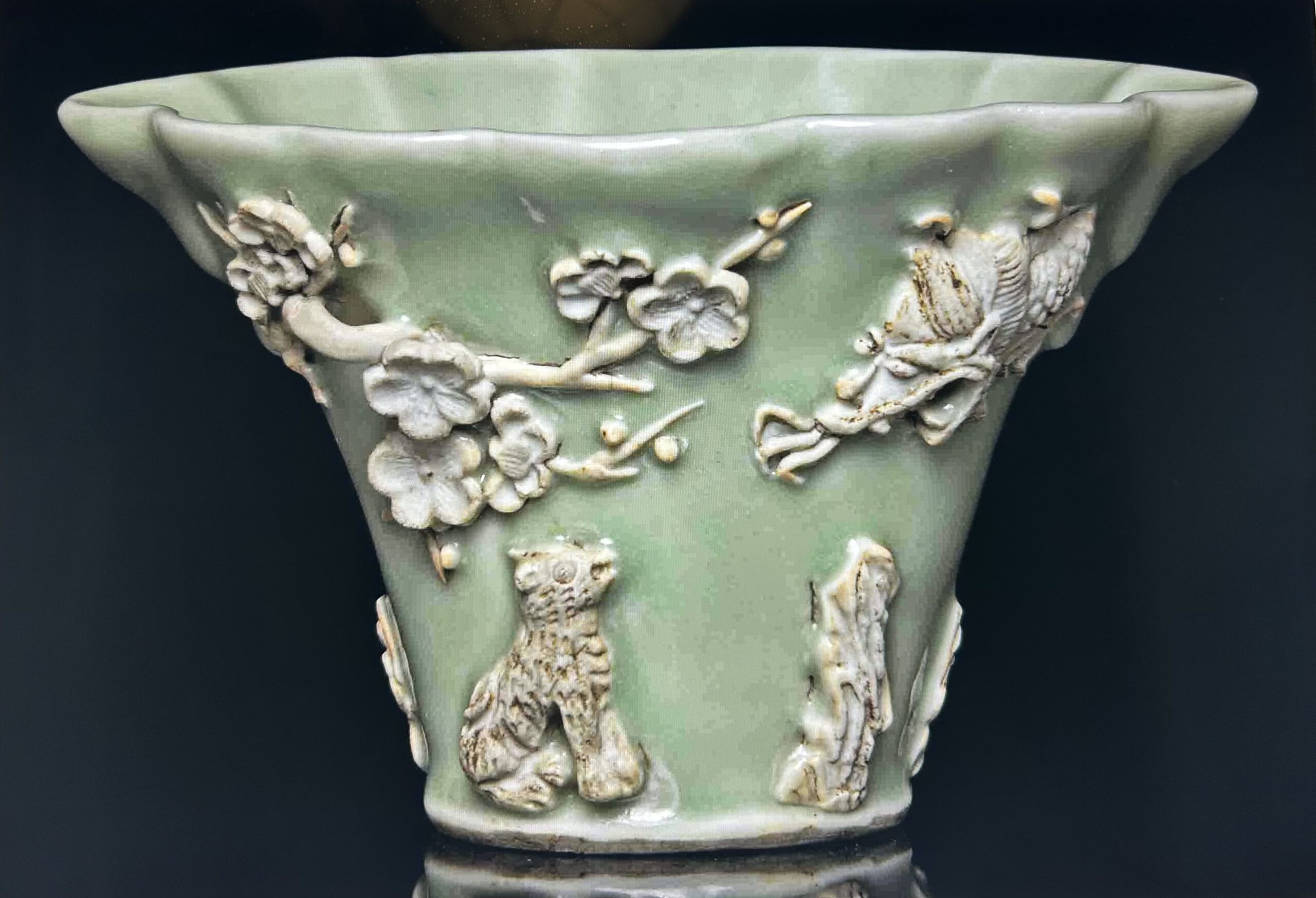 A MOULDED CELADON-GLAZED LIBATION CUPKANGXI PERIOD (1662-1722) Moulded in relief and reserved in the biscuit with a crane flying towards a deer beneath branches of pine on one side, the other side with a lion beneath branches of prunus peering upwards at a dragon emerging from the sky, all reserved on a celadon-glazed ground 5 5/8 in. (14.2 cm.) wide Provenance General Augustus Pitt Rivers (1827-1900) Sale room notice Please note the provenance for this lot should read, General Augustus Pitt Rivers (1827-1900)