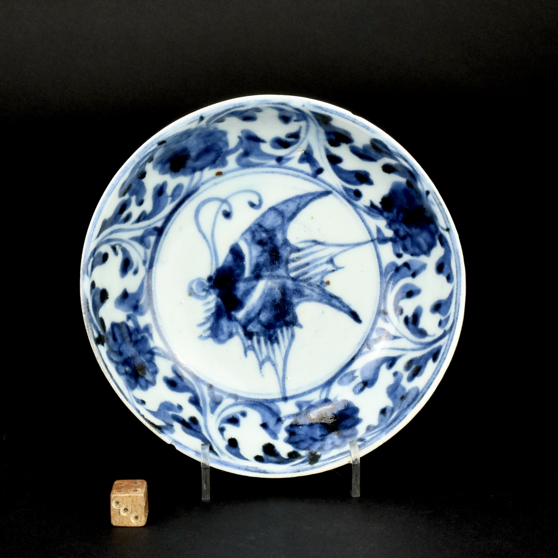 A Rare Shoki-Imari Butterfly Dish, Attributed to the ‘Hyakken Group’ c.1630-1640. This small deep dish, has a heavily potted base which gradually thins to a slightly everted rim. The well is painted with a large butterfly inflight, perhaps a swallowtail butterfly (papilio xuthus), the most common butterfly in Japan. Butterflies, Chō, is principally associated with women and regularly occur on Japanese porcelain but not normally as the central theme. The vigorously painted stylised border, is of a continuous scrolling design with flowers. This dish, and others of this early period, are often painted very freely in a style that could said to relate to painting on pottery. Indeed, many of the people who set up the porcelain industry in Japan from around 1620 were making pottery. This quality of blue is of particularly high quality for this period. There are few pieces of Shoki-imari in European collections, that is because this early Japanese porcelain was not exported to the West. It was made for the Japanese market and is still highly prized in Japan. Dr.Oliver Impey refers to a dish of this design as attributed to the ‘Hyakken Group’ in his group two 1630-1645, see The Early Kilns of Japan, Arita in the First Half of the Seventeenth Century, References above. The Hyakken porcelain kilns started production just before 1630, and continued until around 1650. Kiln wasters have been excavated, but being precise about the attribution to this kiln is often difficult, as one or two other kilns were producing similar pieces. See below for more photographs and references. SOLD Condition Two small rim chips. Size Diameter 14 cm (5 1/2 inches). Depth 4.2 cm (1 1/2 inches) Provenance N/A Stock number 27036 References For a dish of this size and design attributed to the 'Hyakken Group', Impey's group two - 1630-1645, see : The Early Kilns of Japan, Arita in the First Half of the Seventeenth Century (Oliver Impey, Clarendon University Press Oxford 1996. ISBN 0-19-826370-8) plate 20a. Another dish of this design, with the butterfly dark throughout, see : The Azabu Museum of Arts and Crafts, catalogue of 1996, page 87, plate 97 (in Japanese). A set of five of these dishes dated to 1630-1640 are illustrated in : The Kushu Ceramic Museum Collection (The Kyushu Ceramic Museum, Japan March 31st 1987) page 20, plate 15. The title of the book refers to Kushu, when I think they mean Kyushu).