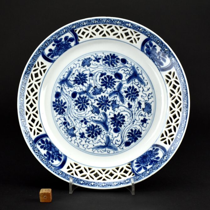 A Kangxi Blue and White Export Porcelain Reticulated Plate c.1690-1720. Objects of this type would have been much more expensive at the time they were made, it involved extra highly skilled work and there would have been more wastage as the cut decoration means they firing process would be more likely to fail. The center is decorated in rich tones of cobalt blue with aquatic plant in water, the border has three cut through panels leaving porcelain in the form of the emblem for wealth, cash. There are four painted panels of flowering plants and a diaper border. The reverse has four ‘Precious Objects’ tied with ribbon. The base has a snail mark. The present piece is an example of what can be referred to as `reticulated` porcelain, reticulated meaning having the form or appearance of a net, it was used as early the beginning of the 18th Century by the famous Père Francois Xavier d`Entrecolles (1664-1741) to describe this type of work on porcelain. Another popular term for this type of pierced or cut decoration is `Devils Work` or Guigong. However the Chinese term Linglong is gradually replacing the previous terms, helped by the publication of Jorge Welsh`s book `Linglong` (Jorge Welsh,London,2004.ISBN 972-99045-2-9). There does not seem to be any difference in the use of terms between the free standing pierced porcelain or that supported by an inner wall, nor a distinction made between the most refined work or the type with larger cut-out sections of porcelain.SOLD Condition In very good condition, some fritting. Warped. Size 21 cm (8 1/4 inches) Provenance N/A Stock number 26554 References For a Kangxi dish of this design in the Groningen Museum, Groningen, Netherlands see : `Linglong` (Jorge Welsh,London,2004.ISBN 972-99045-2-9) page 19, figure 3.