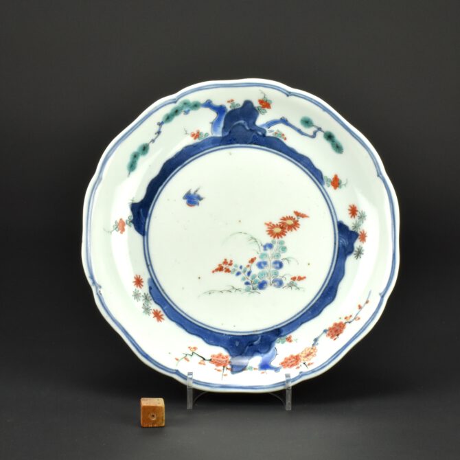 A 17th Century Japanese Kakiemon Porcelain Dish, Kakiemon Kilns or Arita c.1670-1690. This 17th Century foliate dish has underglaze blue and overglaze Kakiemon enamel colours. The design at the center of the dish is of flowering chrysanthemum in enamels. The cavetto is painted with a rocky landscape in underglaze cobalt blue with overglaze decoration of the Three Friends of Winter, Pine, Bamboo and Prunus. The base has an underglaze blue pseudo-Chenghua six-character mark (Ming dynasty 1465-1487). The outer border is in underglaze blue and is a continuous Karakusa scroll designs. A similar dish but with a blue and white landscape to the center is illustrated in the Oriental Ceramics Societie’s catalogue to the exhibition held in the British Museum ; Porcelain for Palaces, The Fashion for Japan in Europe 1650 – 1750 (Various authors, The Oriental Ceramic Society,1990. ISBN 0-903421-24-0) where it is dated to the early 18th century, recent research in Japan points to an earlier date of c.1670-1690. The dish in the catalogue is from the Ashmolean Museum where Dr. Oliver Impey was curator, the notes to the O.C.S. exhibition state that sherds of dishes similar to this have been found at the Kakiemon kiln site, this information probably come from Dr.Impey who was a regular visitor to Japan. See ‘References’.See Below For More Photographs and Information. SOLD Condition In excellent condition, very minimal wear. Size Diameter 18.4 cm (7 1/4 inches). Provenance N/A Stock number 27039 References Complete Catalogue of Shibata Collection (Contributors Saga Kenritsu Kyūshū Tōji Bunkakan. Published by the Kyushu Ceramic Museum, 2019) page 204, plate 1621 for a Kakiemon dish of this type with a phoenix and chrysanthemum to the center. For another Kakiemon dish of this type see Porcelain for Palaces, The Fashion for Japan in Europe 1650 - 1750 (Various authors, The Oriental Ceramic Society,1990. ISBN 0-903421-24-0) page 143, plate 107. 