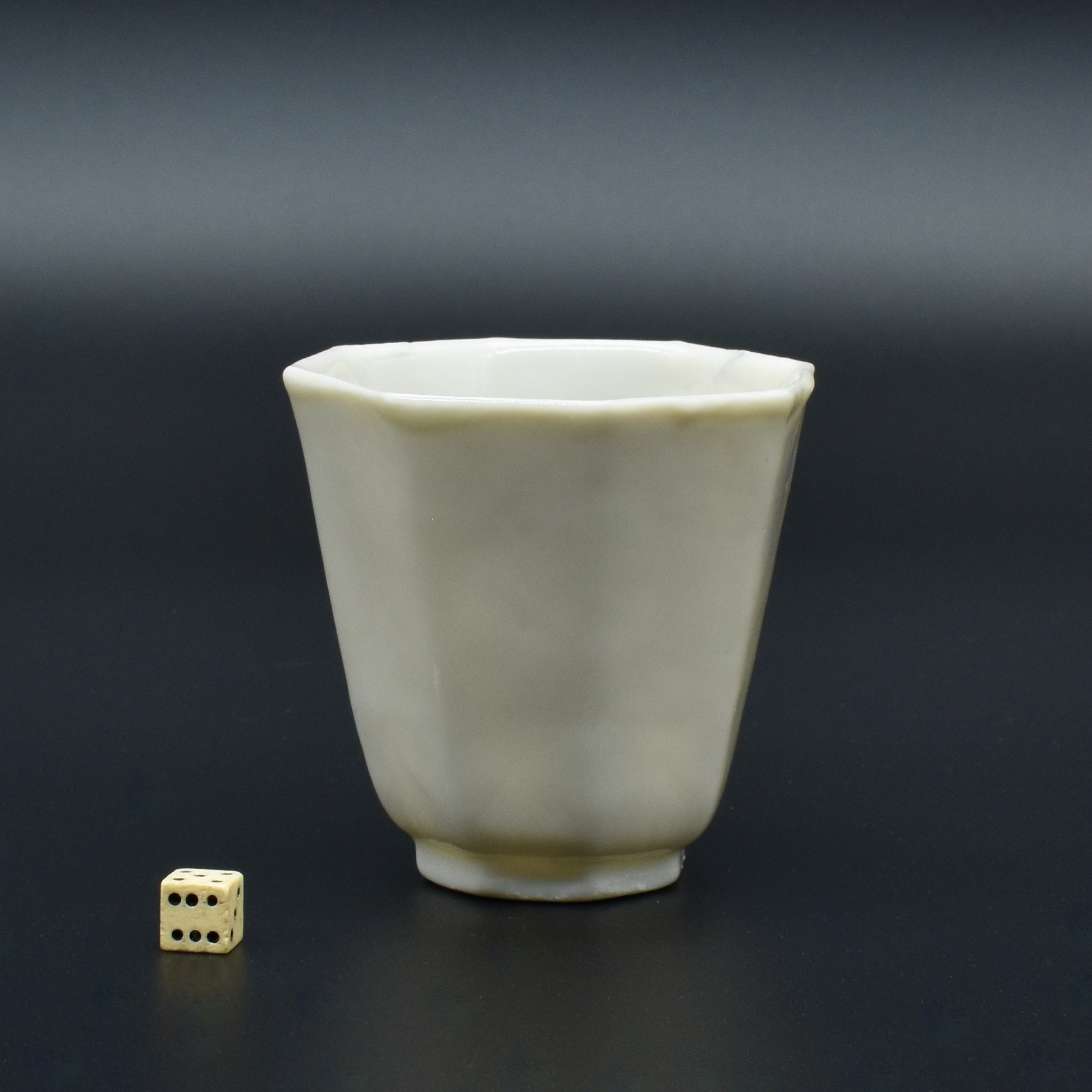 A Kangxi Octagonal Blanc de Chine Porcelain Beaker, Dehua kilns, Fujian Province c.1680 - 1720. The lower curved part of each panel has a lotus form lappet which has been moulded, the base has a raised seal-mark (see the additional photographs in the Photograph Gallery below). This simple form is rather more unusual than the other more thickly potted moulded examples, many of which bare a seal-mark for the workshop Zhongtun shi (Mr. Zhongtun). See below for a plain Blanc de Chine example and a beaker with enamel decorated added in London in around 1715 to 1720.Blanc de Chine Porcelain : The porcelain known in the West as Blanc de Chine was produced 300 miles south of the main Chinese kiln complex of Jingdezhen. The term refers to the fine grain white porcelain made at the kilns situated near Dehua in the coastal province of Fujian, these kilns also produced other types of porcelain. A rather freely painted blue and white ware, porcelain with brightly coloured `Swatow` type enamels as well as pieces with a brown iron-rich glaze. However it is the white Blanc de Chine wares that have made these kilns famous. The quality and colour achieved by the Dehua potters was partly due to the local porcelain stone, it was unusually pure and was used without kaolin being added. This, combined with a low iron content and other chemical factors within the body as well as the glaze, enabled the potters to produce superb ivory-white porcelain.