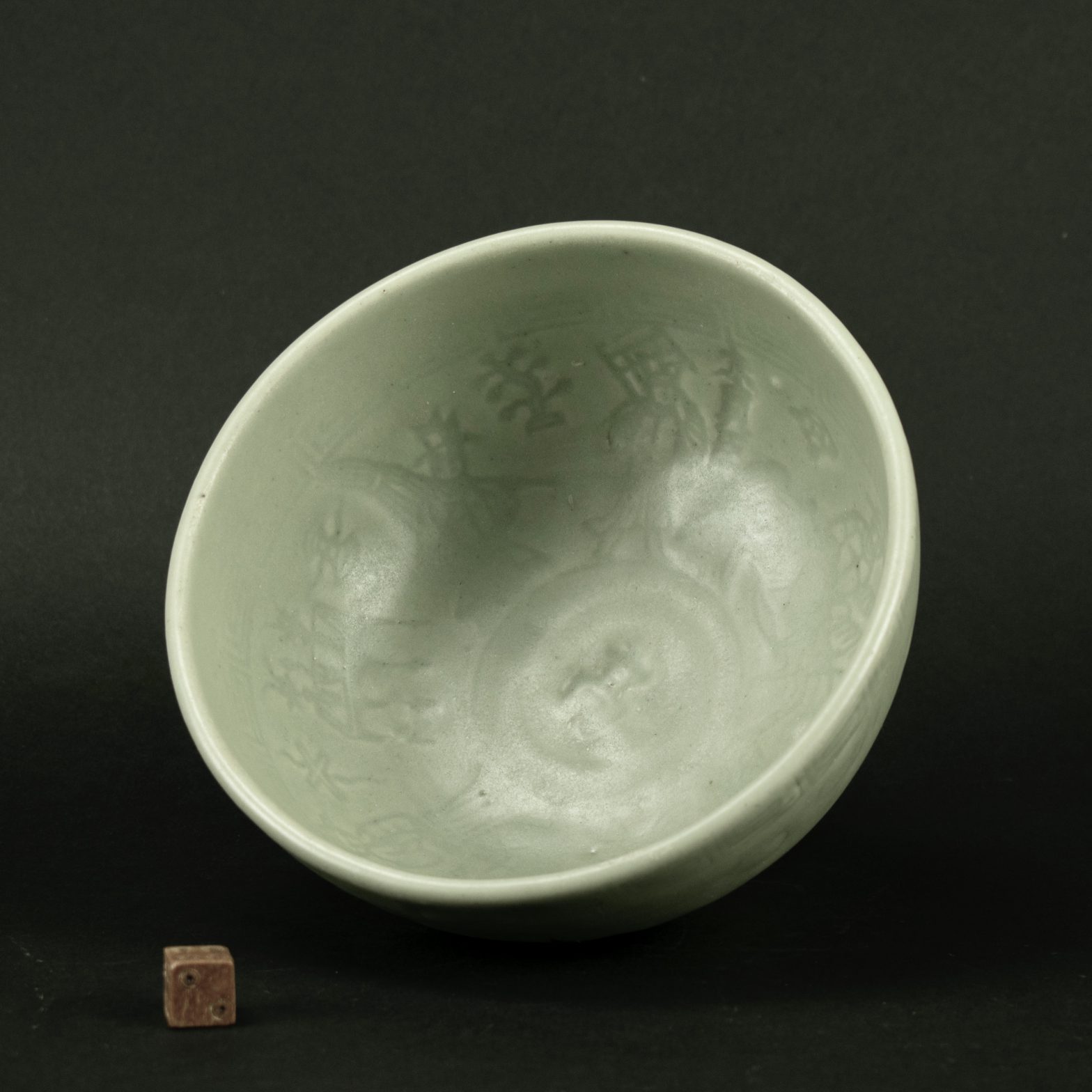 An Early Ming Celadon Bowl, Longquan Kilns, Late 14th or Early 15th Century. The interior of this Ningyo ude celadon bowl is lightly moulded with figures with explanatory inscriptions and a `Greek-Key` border above, the well is Impressed with a single character. The border design is repeated on the exterior, below it are quickly incised flowering plants. The bowl is covered in a very thick glaze and much of the detail is clear. There is a man on horseback accompanied by his companions and an alter table with two vases and a censer.This bowl and its companion are from a Japanese collection. A similar Ming celadon bowl was discovered in the ruins of Saya Castle, Komatsu-Shi, Ishikawa prefecture, Japan, built in the sixteenth century, and now in the Tokyo National Museum. Such bowls are called Ningyo ude bowls in Japan because of their figural decoration. See below for more information about this group of early Ming celadon bowls and examples of kiln wasters. See Below For More Photographs and References. SOLD Condition In good condition, the exterior of the foot has two old glaze cracks. The glaze is slightly dry and of a semi-matt appearance. Size Diameter : 14.9 cm (6 inches). Height : 8.8 cm (3 1/2 inches). Provenance A Japanese ink inscription on the base states that this Ming bowl was one of a pair, see the other bowl, stock number 25279 Stock number 25280 References Several examples of this type are known. A bowl which of a good rich colour and of a different design is illustrated in : Yuegutang, A Collection of Chinese Ceramics in Berlin (Regina Krahl, G+H Verlag, Berlin, 2000) pages 280 and 280. A similar but Ming celadon bowl of this type is in the British Museum see : Ming Ceramics in the British Museum (Jessica Harrison-Hall, British Museum Press, 2001) page 482, Item 16:52. A further example of this type of Ming celadon bowl was discovered in the ruins of Saya Castle, Komatsu-Shi, Ishikawa prefecture, Japan, built in the sixteenth century, and now in the Tokyo National Museum. Such bowls are called Ningyo ude bowls in Japan because of their figural decoration". For another example of this type of Ming Celadon Bowl see : Chinese Ceramics, Bronzes and Jades in the Collection of Sir Allan and Lady Barlow (Michael Sullivan, Faber and Faber Ltd, 1963) page 99, illustration 95c ; `Chekiang Celadon, XIV-XV Century`. Also see : Chinese Ceramics, The New Standard Guide (Hi Li,Thames and Hudson,1996) pages 246 and 262, item 510, "The decoration of this bowl, combining calligraphy with human figures, reflects a new trend in Longquan (celadon) products during the Ming dynasty. In addition to the auspicious phrases and names of potters that had increasingly appeared on Longquan wares since the Yuan, historical figures provided another rich resource for decorative motifs at Daotai and Daqi (kilns at Zheijiang).