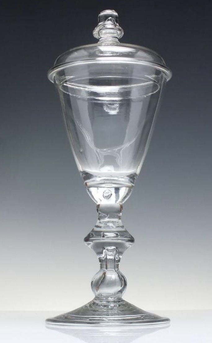 Dated to around 1690, this English lead-glass vessel has a cover, a hollow pillar stem and a folded foot. The museum suggests possible connections with glassmakers George Ravenscroft or Hawley Bishopp, though the attribution is uncertain.